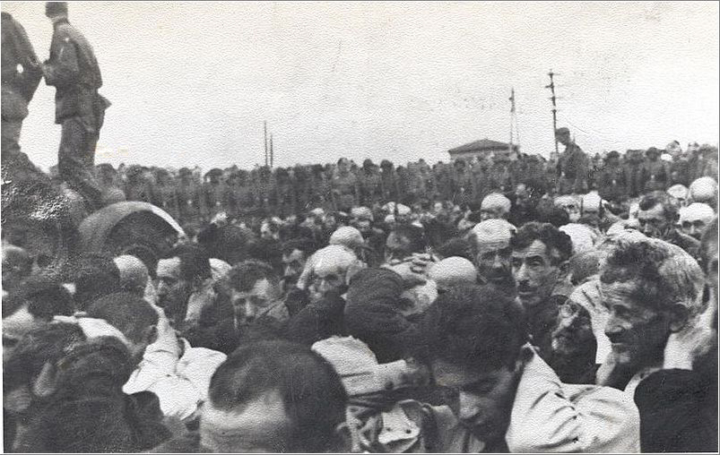 Liquidation of the Białystok ghetto, 15–20 August 1943. A Jewish crowd outside stands with its hands up and watched by an Axis military unit.