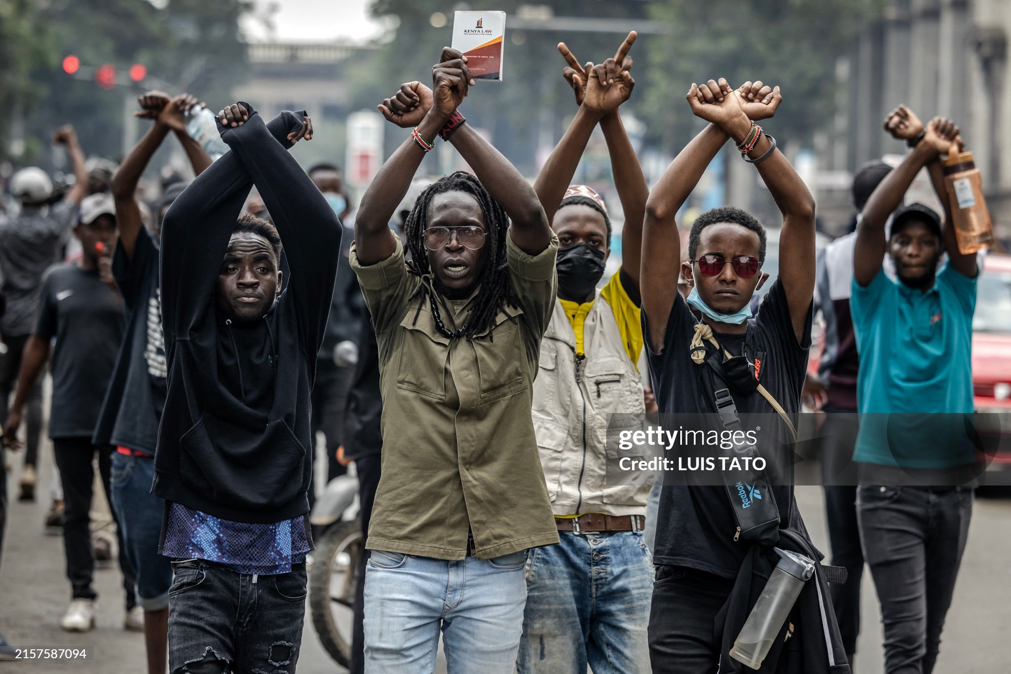 Protesters make signs with their arms in front of Kenya police officers during a demonstration against tax hikes as Members of the Parliament debate the Finance Bill 2024 in downtown Nairobi, on June 18, 2024.