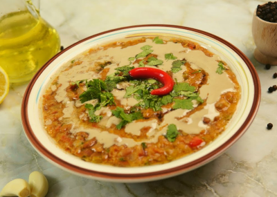 A dish of Ful Medames with tahini and a bright red chili pepper in the middle