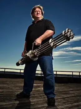 Gabe Newell engaging his inner heavy weapons guy , by standing on some dock looking thing , bolding a machine gun